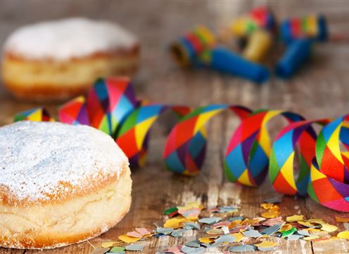 Ein paar leckere Krapfen mit Puderzucker stehen auf einem Holztisch. Bunte Konfetti und Luftschlangen dekorieren die Umgebung für eine Feier.