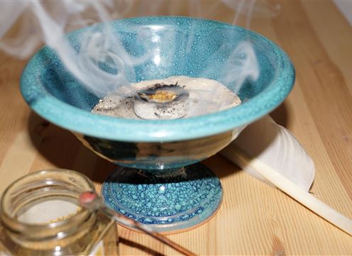 Eine schöne Schale mit Rauch und einer verbrannten Substanz. Daneben befindet sich ein Glas und eine Feder.
