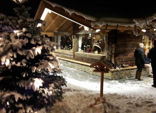 Ein gemütlicher Holzschuppen unter einem klaren Nachthimmel, umgeben von schneebedeckten Bäumen. Lichter funkeln und schaffen eine festliche Atmosphäre.