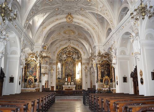Een prachtige kerk met een hoge gewelven en kunstzinnige muurschilderingen. De houten banken staan in rechte rijen voor het altaar.