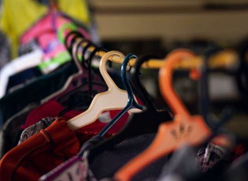 Ein Kleiderbügel mit verschiedenen Kleidungsstücken hängt auf einer Stange. Die Farben der Kleidung sind lebhaft und abwechslungsreich.