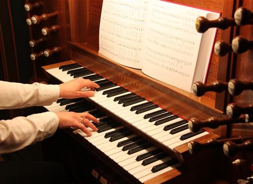 A person is playing the piano with both hands on an elegant keyboard. Sheet music is visible in the background.