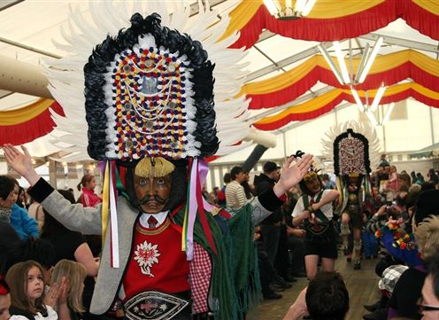 A festive parade with people in colorful traditional costumes and large hats. There is a lot going on, and the crowd is enthusiastically applauding.