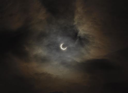 A dark sky with clouds and a partial lunar eclipse. The moon appears thin and emits faint light.