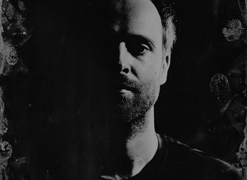 Een monochroom portret van een persoon met een gedeeltelijk verlicht gezicht. De achtergrond is donker en onscherp, wat de focus op de gelaatstrekken legt.