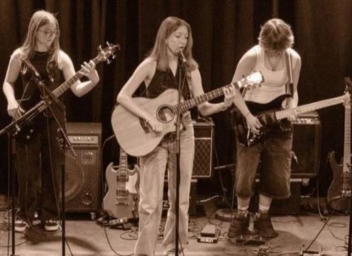 Eine Band tritt auf der Bühne auf. Die Musikerinnen spielen Gitarre und Bass in einem abgedunkelten Raum mit farbigem Licht.