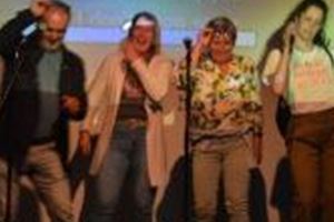 A group of four people is standing in front of a screen and singing enthusiastically. They look happy and are having fun at karaoke.