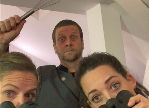 Drei Personen halten Ferngläser und schauen neugierig in die Kamera. Eine Person hält einen Schneebesen in der Hand und hat einen überraschten Gesichtsausdruck.