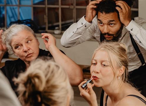 A group of people is getting ready for an event. Some are doing their hair while another person is applying lipstick.