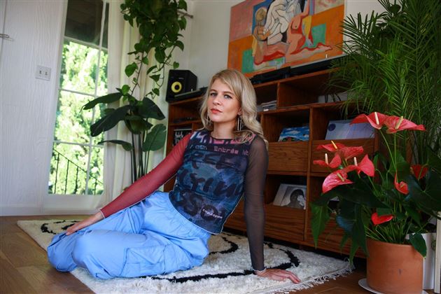 Une personne tient une ananas devant son visage et porte des écouteurs. L'arrière-plan est blanc et clair.