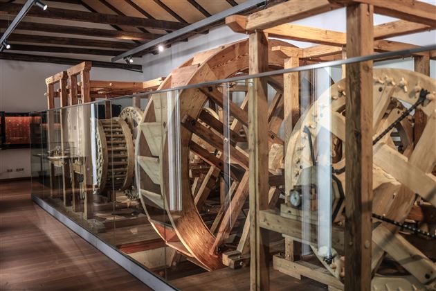 Ein historisches Wasserrad aus Holz in einem Ausstellungsraum. Es ist hinter Glasvitrinen sichtbar und zeigt detaillierte handwerkliche Konstruktionen.