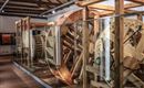 Ein historisches Wasserrad aus Holz in einem Ausstellungsraum. Es ist hinter Glasvitrinen sichtbar und zeigt detaillierte handwerkliche Konstruktionen.