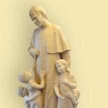 A statue of a man gently surrounded by children. He wears a long robe and appears to be friendly.