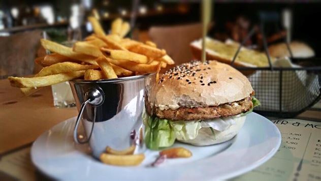 Ein leckerer Burger mit Sesambrötchen und frischem Salat, serviert mit knusprigen Pommes in einem kleinen Eimer. Der Teller hat eine ansprechende Präsentation und lädt zum Genießen ein.