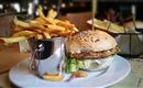 Ein leckerer Burger mit Sesambrötchen und frischem Salat, serviert mit knusprigen Pommes in einem kleinen Eimer. Der Teller hat eine ansprechende Präsentation und lädt zum Genießen ein.