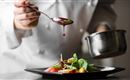 A chef decorates a salad with a sauce. The dish is presented on a black plate.
