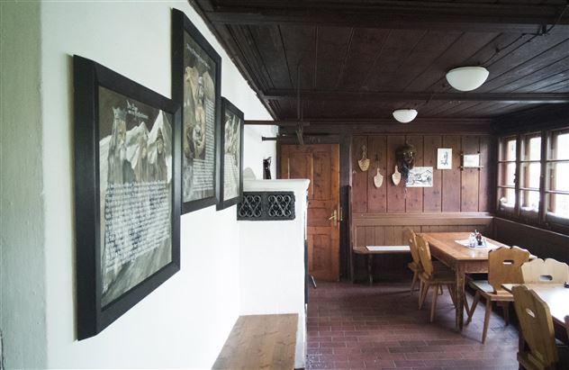 Een gezellige eetkamer met houten wandbekleding en een grote eettafel. Aan de muur hangen verschillende foto's en decoraties.