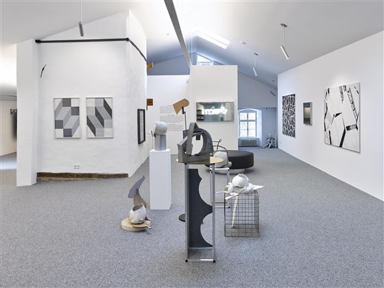 Un musée d'art moderne avec des objets sculpturaux et de la peinture abstraite. Les murs sont clairs et les espaces semblent ouverts et accueillants.