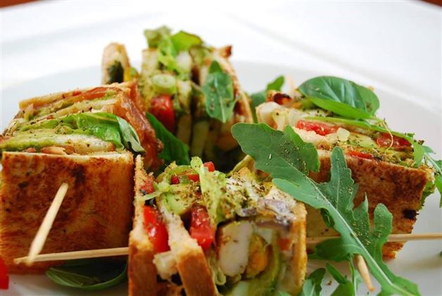A delicious sandwich platter with fresh vegetables and salad. The sandwiches are beautifully arranged and secured with toothpicks.