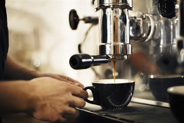 Eine Person bereitet einen Espresso mit einer Kaffeemaschine vor. Der Kaffee läuft in eine schwarze Tasse.