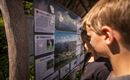 Zwei Kinder betrachten ein Informationsschild über die Natur. Das Schild enthält Bilder und Texte zu verschiedenen ökologischen Themen.