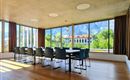 Ein moderner Konferenzraum mit einem großen Tisch und Stühlen. Durch die Fenster ist eine grüne Landschaft und Berge sichtbar.