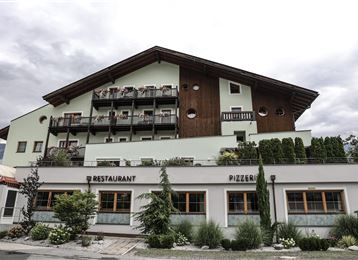 Un grand bâtiment avec des éléments en bois et plusieurs balcons. En bas se trouvent un restaurant et une pizzeria.