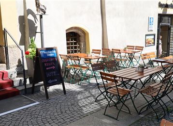 Un accogliente spazio all'aperto di un caffè con sedie e tavoli in legno. L'ambiente è luminoso e invitante, ideale per una pausa all'aperto.