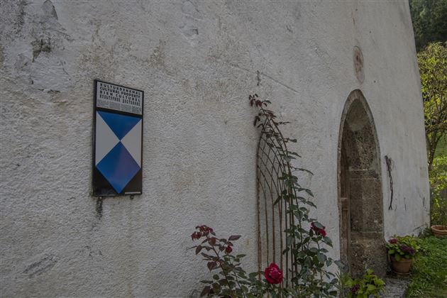 Een wit gebouw met een groene omgeving. Aan de muur is een symbool zichtbaar in blauwe en witte kleuren, evenals een ingang.