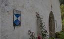 Een wit gebouw met een groene omgeving. Aan de muur is een symbool zichtbaar in blauwe en witte kleuren, evenals een ingang.
