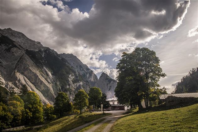 Een schilderachtig berglandschap met hoge bergen en een zachte groene weide. Op de achtergrond zijn er wolken en bomen te zien die een rustige sfeer creëren.