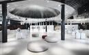 Un negozio moderno ed elegante con un grande elemento a cupola nel soffitto. Sedute rotonde e un arredo luminoso e minimalista creano un'atmosfera accogliente.