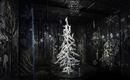 Un albero di Natale bianco e luminoso si trova in una stanza buia con motivi murali creativi e grafici. Attorno all'albero sono appese decorazioni simili alla neve e fiocchi di neve.