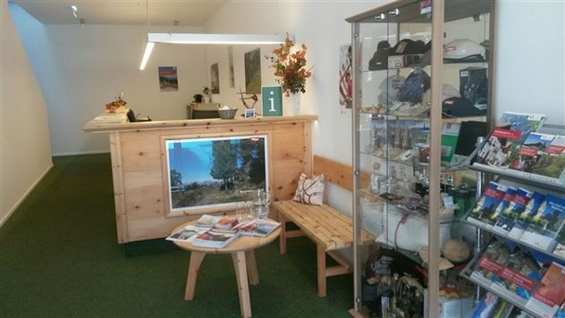 Un hall d'accueil avec un comptoir en bois et du matériel d'information. Sur une table, des brochures sont disposées et un grand panneau affiche un beau paysage.