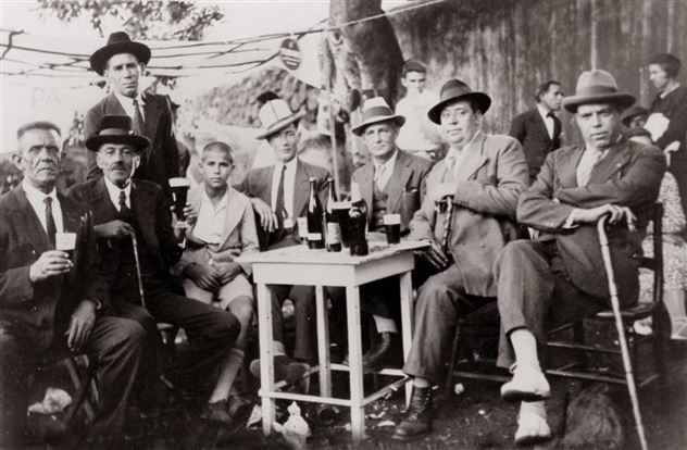 A group of men and a boy is sitting around a table with drinks. They are all wearing hats and seem to be having a sociable time.