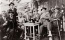 A group of men and a boy is sitting around a table with drinks. They are all wearing hats and seem to be having a sociable time.