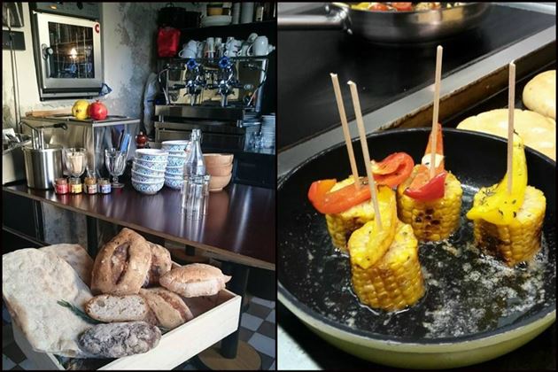 A cozy café with a counter full of drinks and fresh bread. On the other side, grilled corn on the cob with colorful vegetables can be seen.