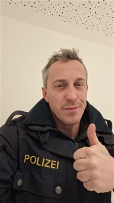 Ein Mann in einer Polizeijacke gibt einen Daumen hoch. Der Hintergrund ist schlicht und hell.