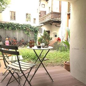 Ein gemütlicher Innenhof mit einem kleinen Tisch und Stühlen. Im Hintergrund sieht man Fahrräder und Pflanzen.