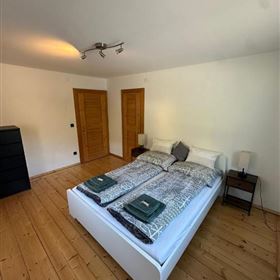 Una camera da letto moderna con un grande letto e pavimento in legno. Le pareti sono bianche e c'è un arredamento semplice ed elegante.