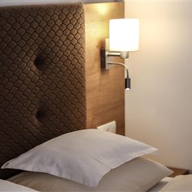 Ein gemütliches Bett mit weißen Kissen und einem stilvollen Nachttischlicht. Die Wand hinter dem Bett hat ein elegantes Design.