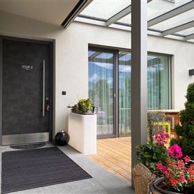 Een moderne ingang met een zwarte voordeur en grote ramen. Kleurrijke bloemen en planten geven de ingang een uitnodigende sfeer.