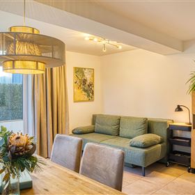 Un salon moderne avec un canapé vert et une table à manger en bois. De grandes fenêtres laissent entrer beaucoup de lumière naturelle et créent une atmosphère agréable.