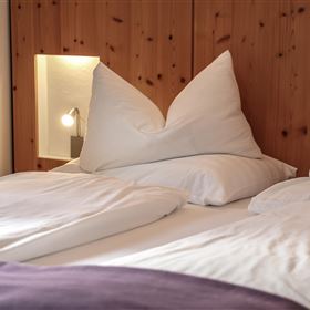 Ein gemütliches Schlafzimmer mit einem Doppelbett und großen, geschwungenen Kissen. Die Wände sind aus Holz und es gibt eine sanfte Beleuchtung.