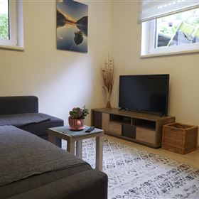 A cozy living room with a gray sofa and a television. A small table and two chairs complement the furnishings.