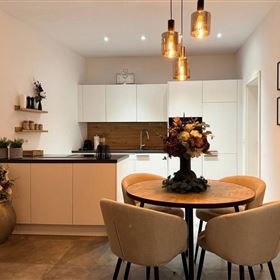 Moderne Küche mit einem runden Tisch und bequemen Stühlen. Dekorative Pflanzen und geräumige Möbel schaffen eine einladende Atmosphäre.