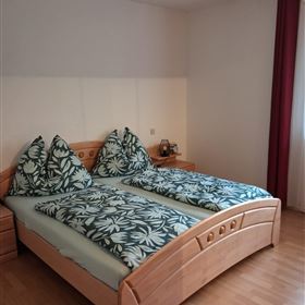 Een gezellige slaapkamer met twee bedden en kleurrijke kussens. Het houten meubilair en de warme vloer geven de ruimte een uitnodigende sfeer.