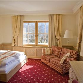 Una camera d'hotel accogliente con un letto matrimoniale e un tappeto rosso. Un divano e grandi finestre garantiscono molta luce naturale.