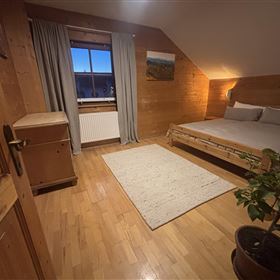 A cozy bedroom with wood paneling and a large bed. The room is brightly lit and has a plant in a pot.