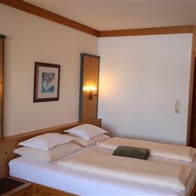 Ein gemütliches Schlafzimmer mit einem Doppelbett und Holzvertäfelung. Die Wände sind hell, und es gibt zwei Wandleuchten für eine angenehme Beleuchtung.